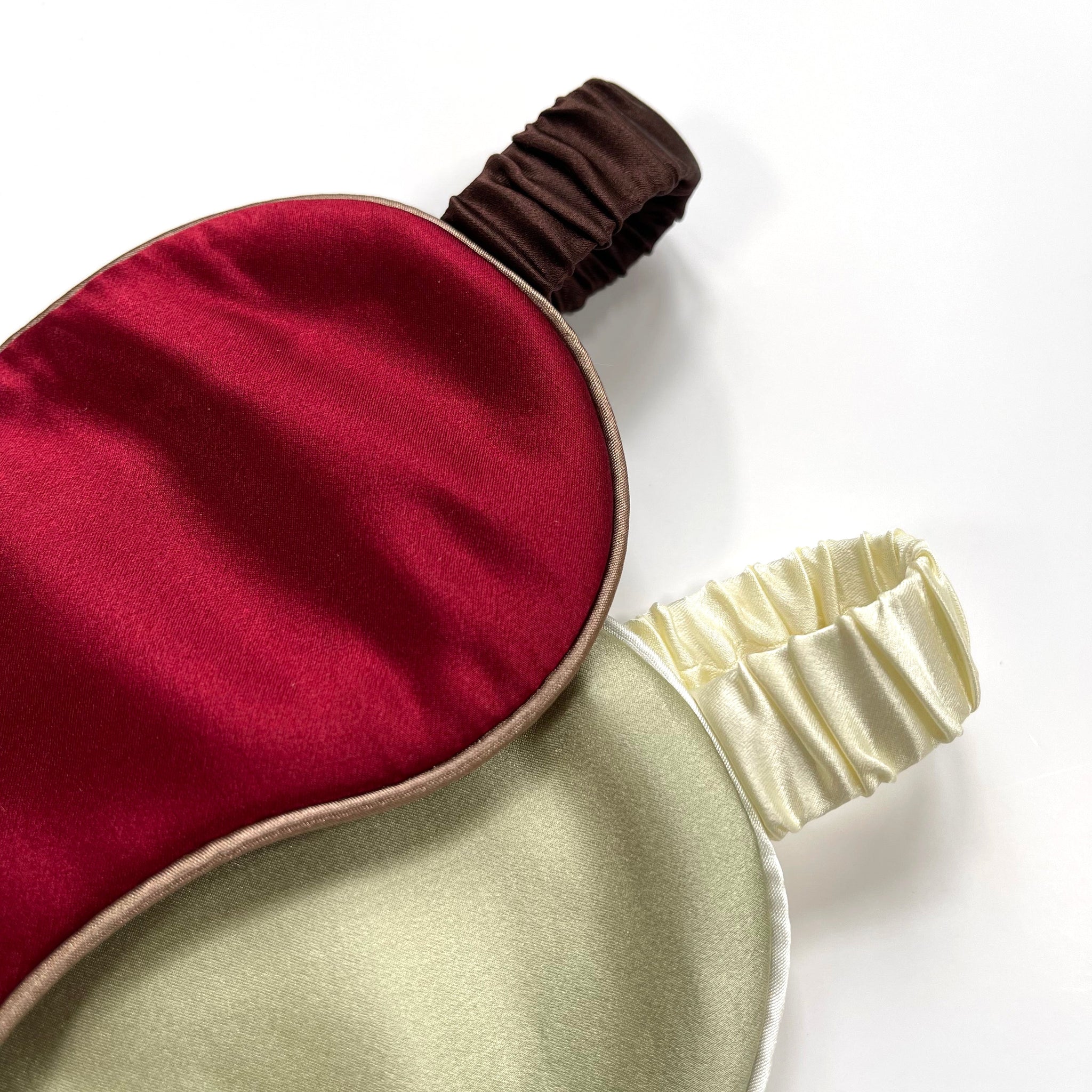 a red silk eye mask with brown strap and a pea green silk eye mask with creamy white strap