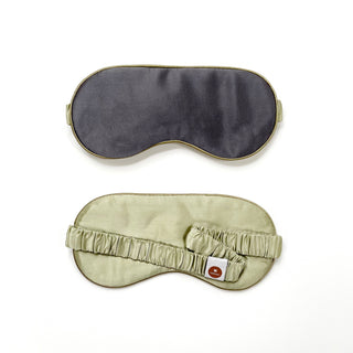 Double-sided silk sleep mask featuring dark gray fabric with gold trim on one side and caramel gold with elastic band on the reverse, showing luxury design