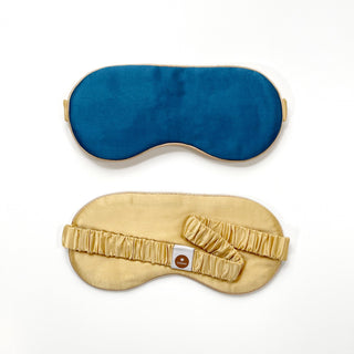 Luxury double-sided silk sleep mask featuring deep blue on one side and caramel gold on the other with elastic band and brand tag