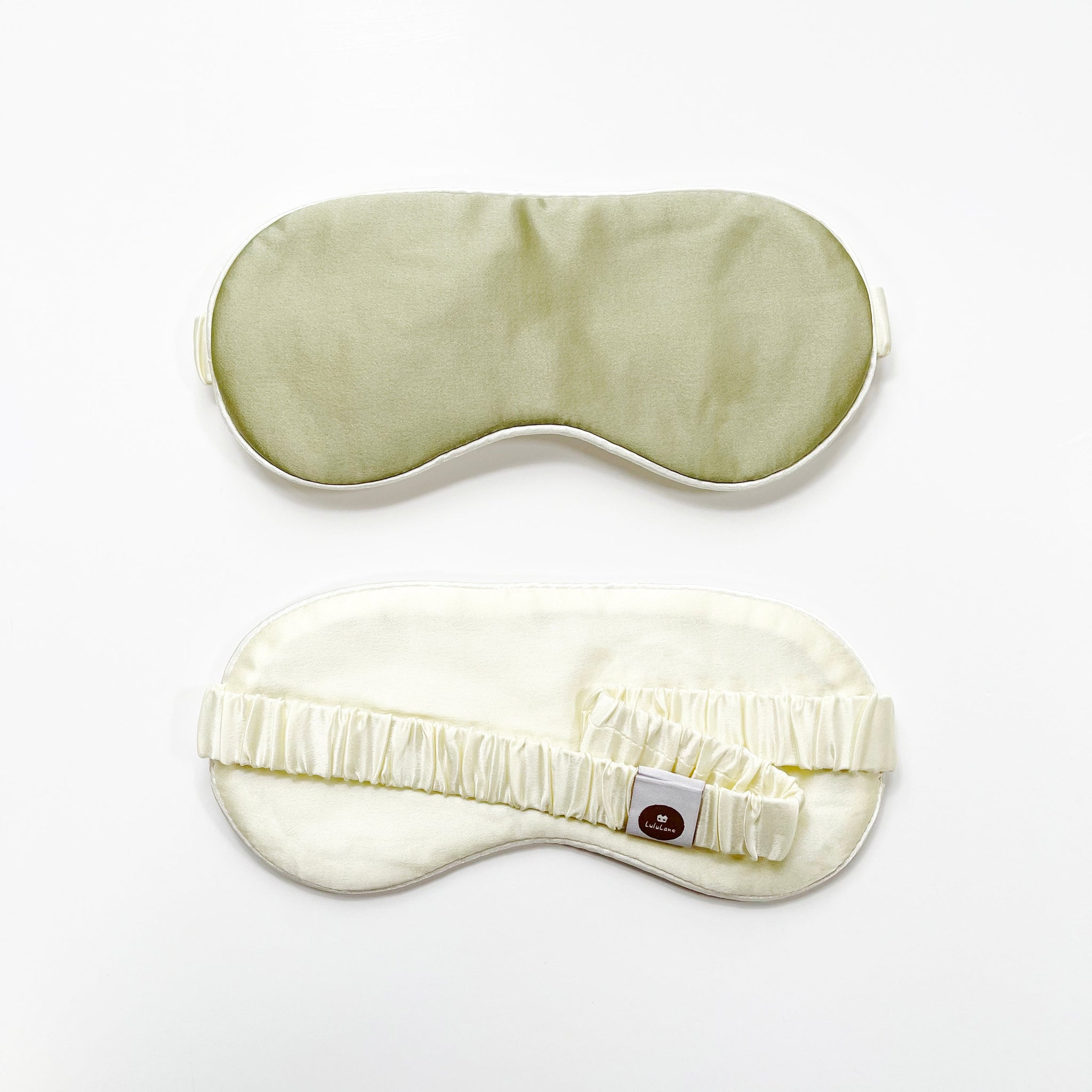 a pea green silk eye mask with creamy white back side and elastic strap