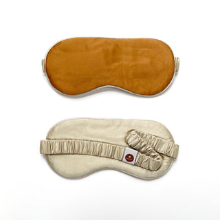 Double-sided luxury sleep mask showing caramel brown top side and cream-colored underside with elastic band and small brand tag, designed for comfort.