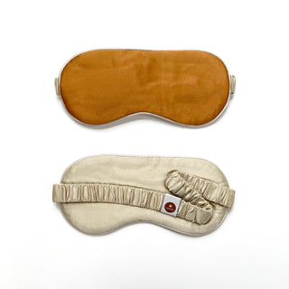 Luxury double-sided silk sleep mask featuring amber gold on one side and cream silk on reverse with elastic strap and brand logo tag