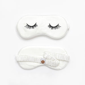a white silk eye mask featuring black eyelashes embroidery and elastic strap
